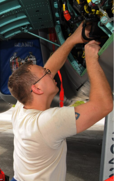 man in glasses adjusts mechanical components of an airplane